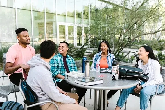 5 students sitting at an outdoor table on campus