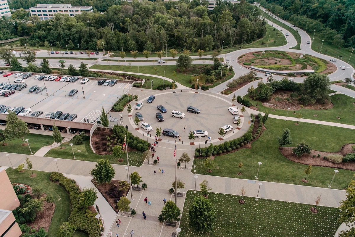 An aerial view of a busy parking area with a circular driveway, surrounded by green spaces and roads.