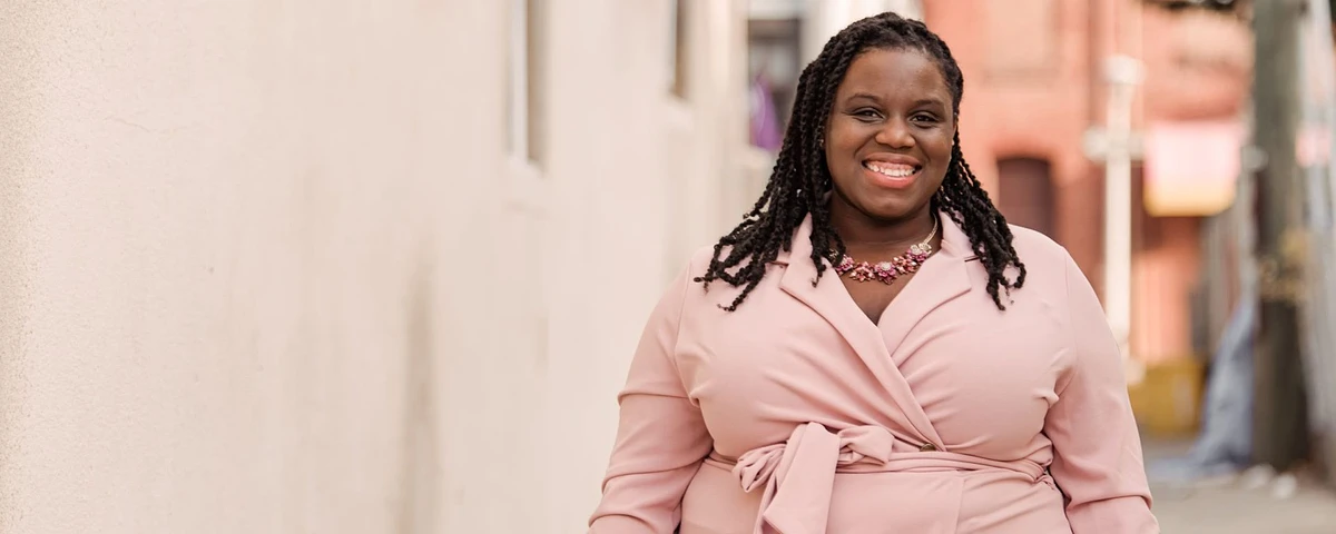 Individual smiling in a pink dress in front of a white building